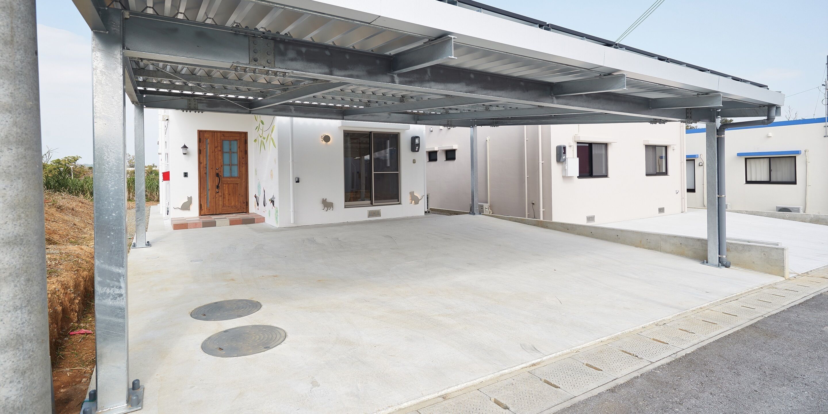 A covered outdoor area with a concrete floor, a metal roof, and a building entrance with a wooden door and windows.