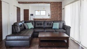 Ein modernes Wohnzimmer mit einem Ecksofa, einem Couchtisch aus Holz und einer Küche im Hintergrund.