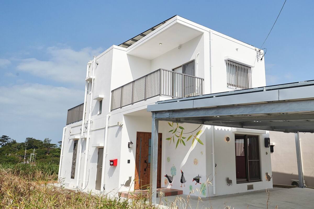 A modern two-story house with a balcony, a covered porch, and a small garden area.