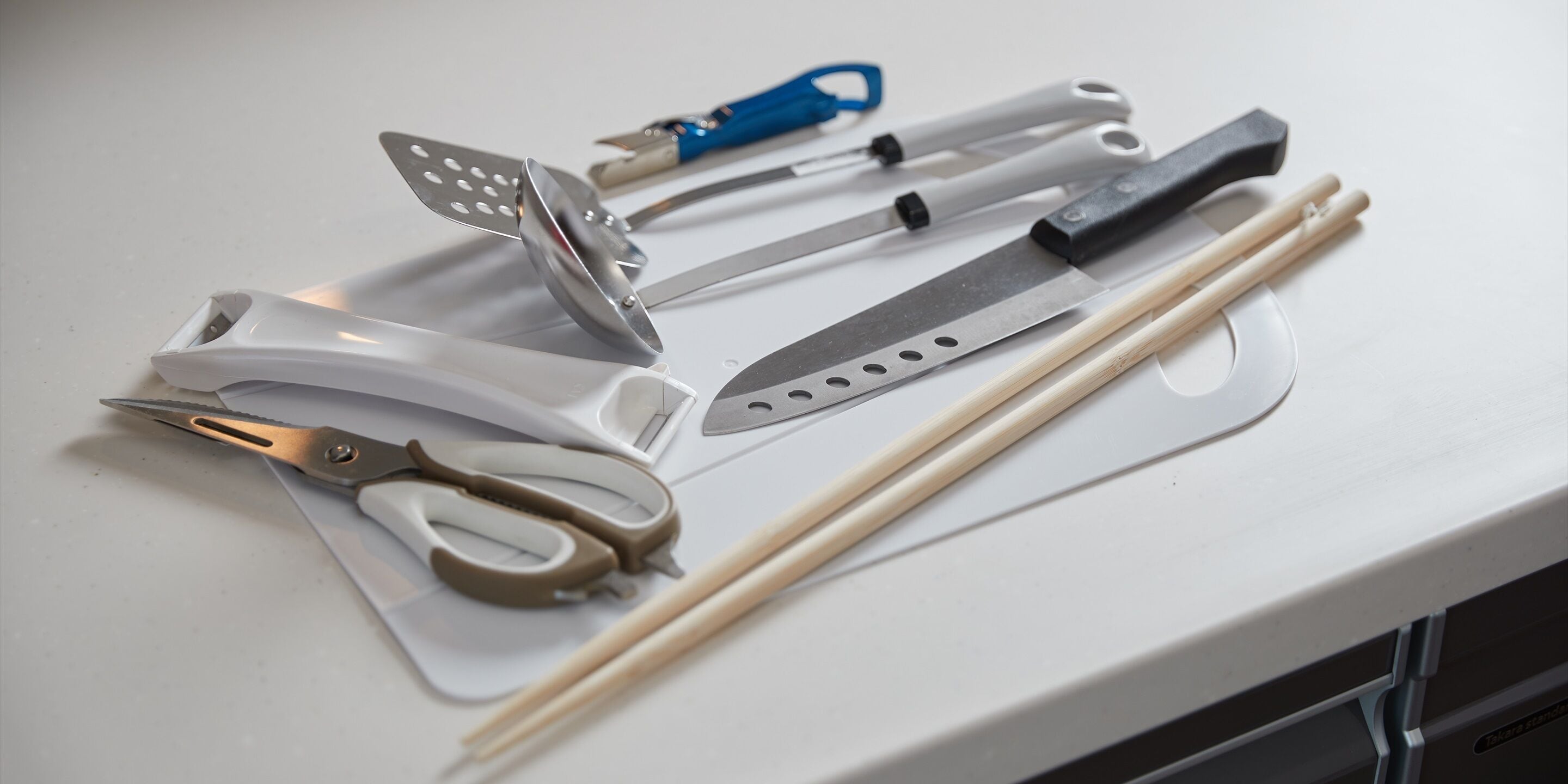 A kitchen counter with various utensils including scissors, a grater, a knife, and chopsticks.