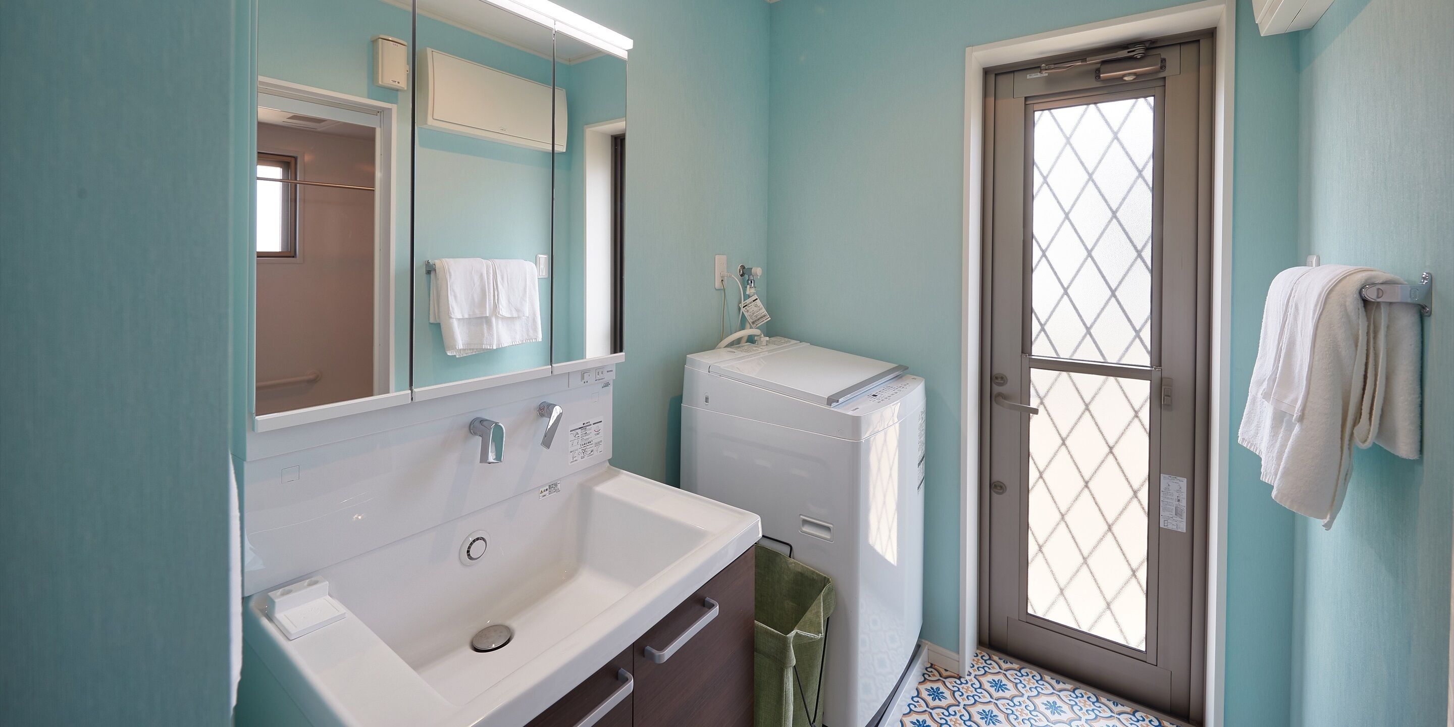 A bathroom with a white sink, a mirror, a window with a grid pattern, and a door.