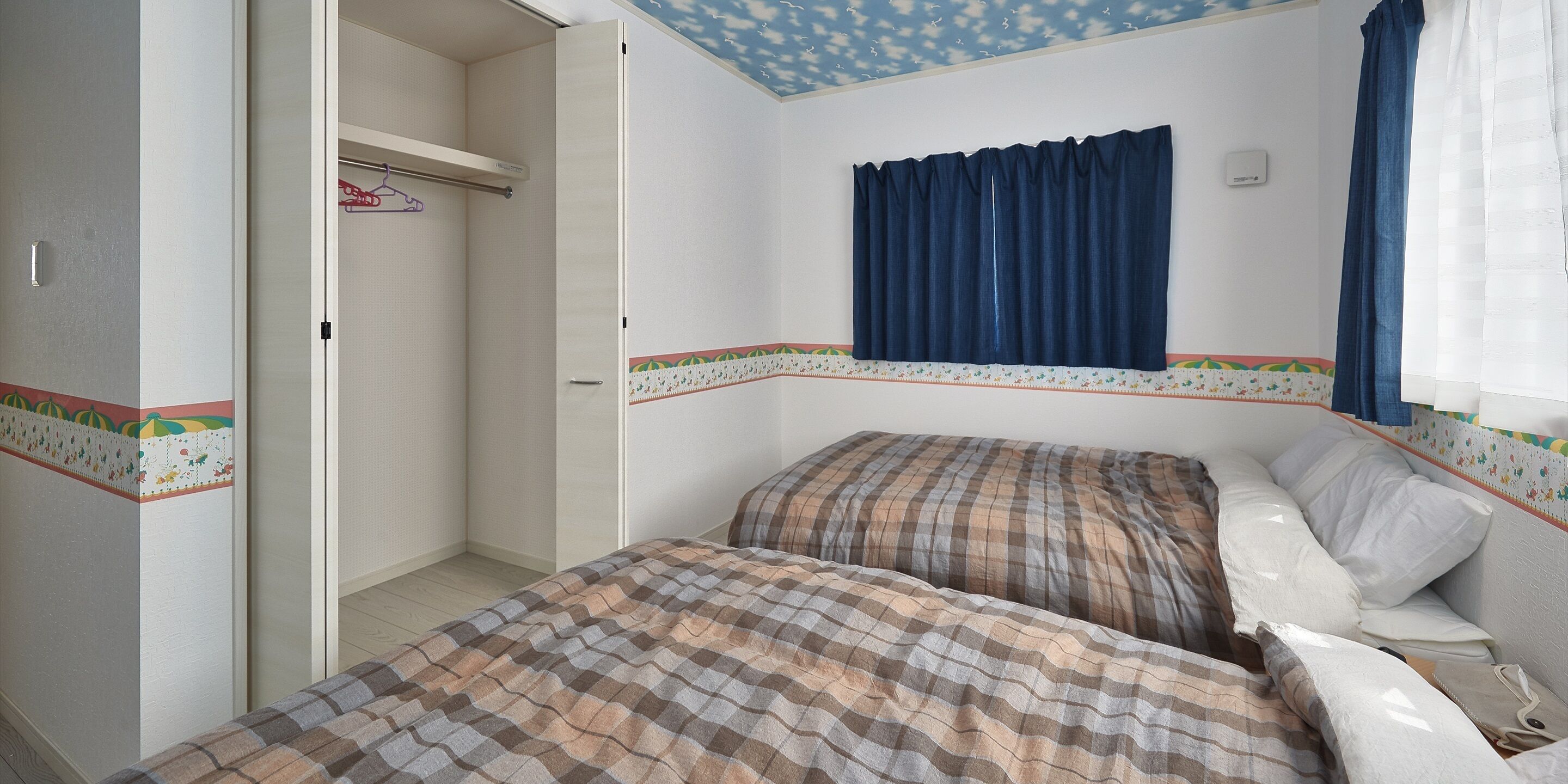 Un dormitorio con dos camas, un armario, una ventana con cortinas azules y un techo con diseño de nubes.