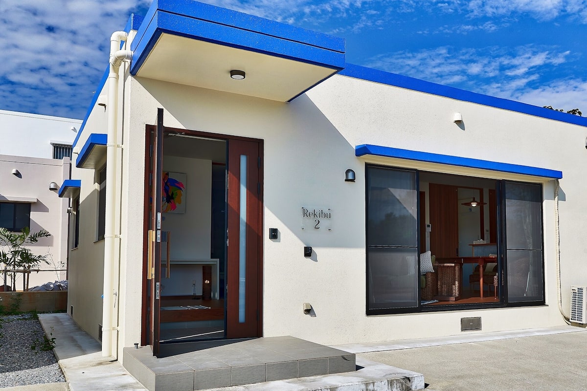 A modern building with a blue and white facade, a large window, and a door.