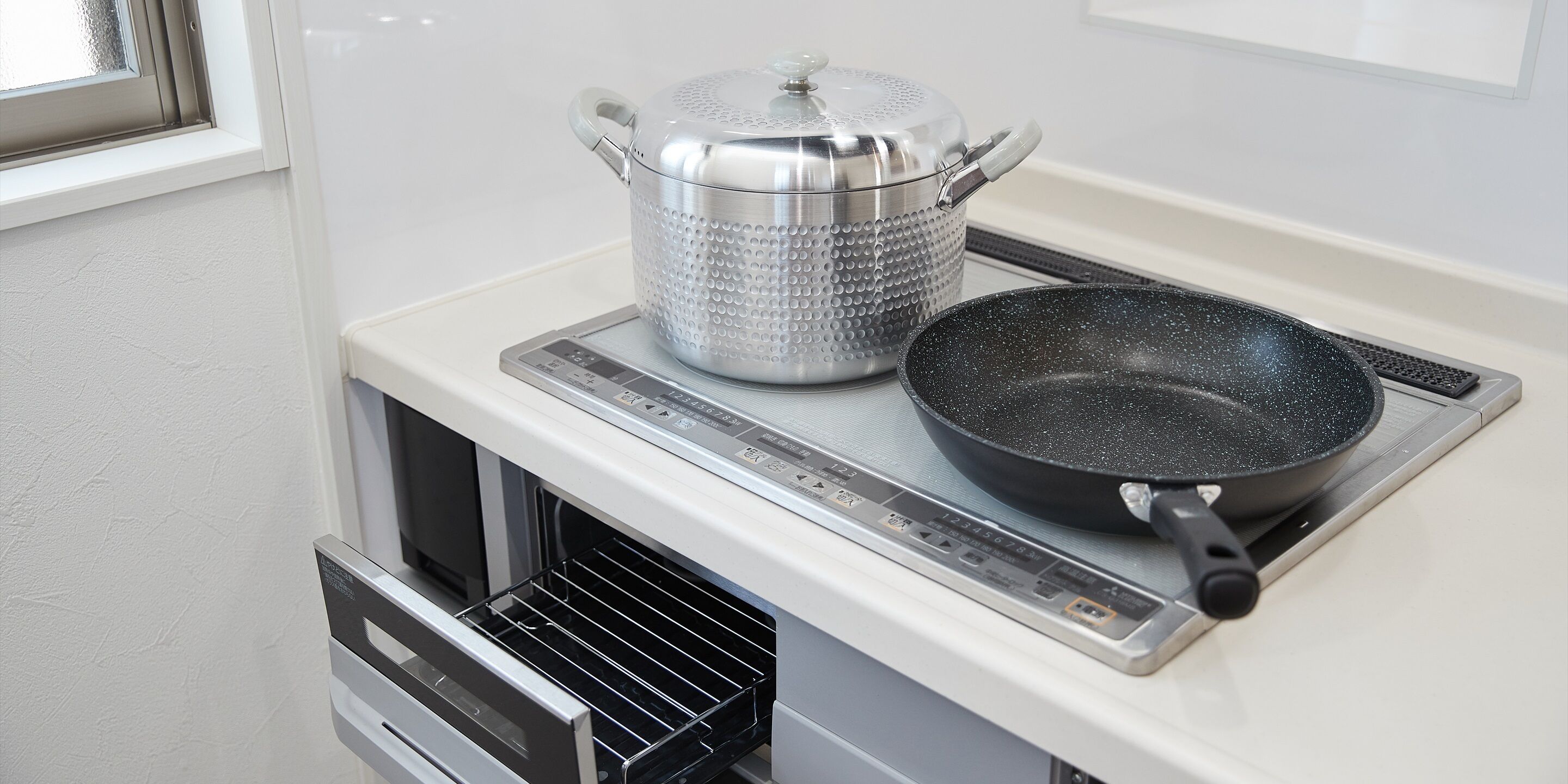 A kitchen with a stainless steel pot on a portable induction cooktop and a frying pan.