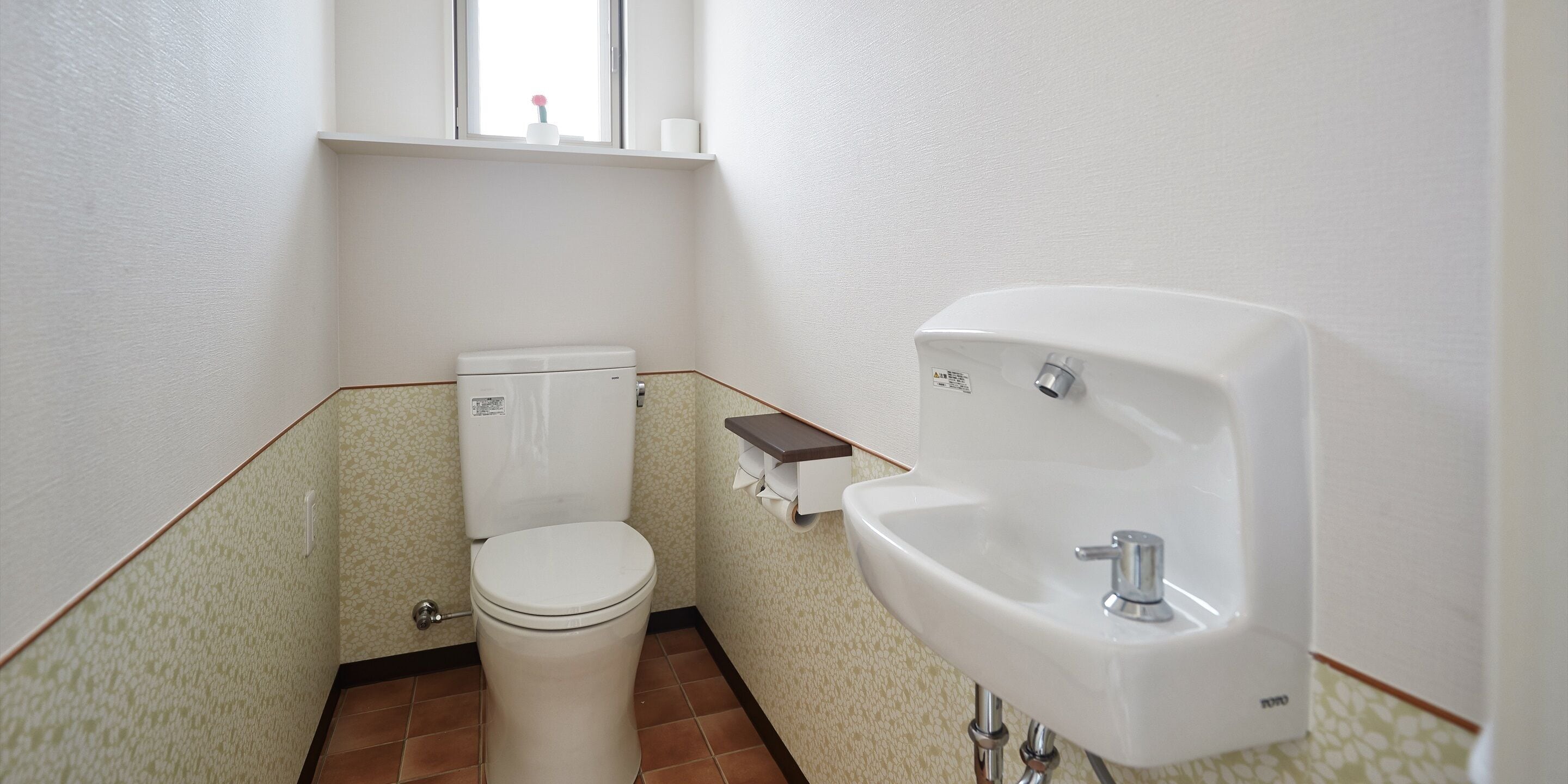 A small bathroom with a toilet, a sink, and a window above the toilet.