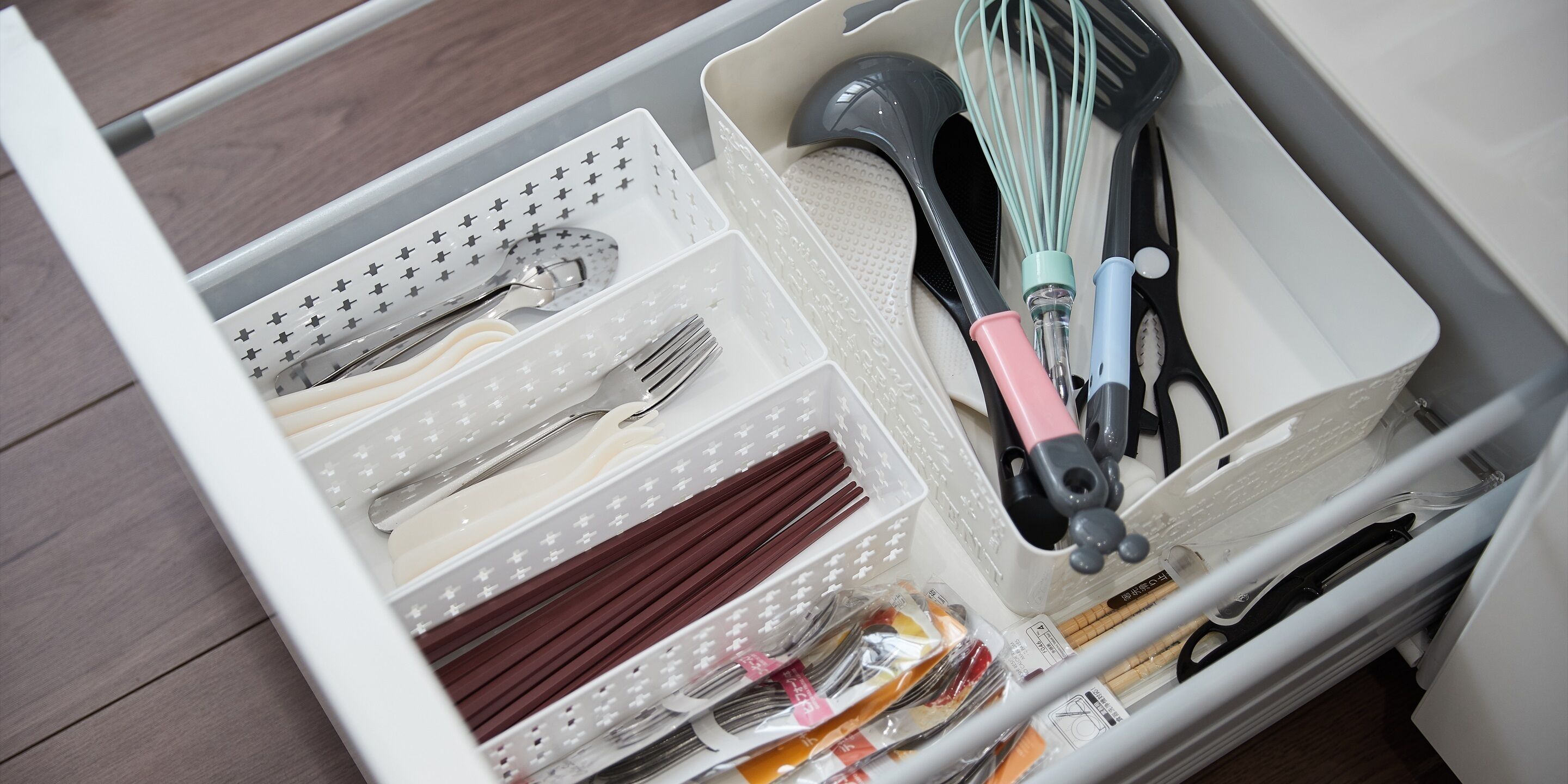 A drawer with compartments containing kitchen utensils, including spoons, forks, chopsticks, and a whisk.