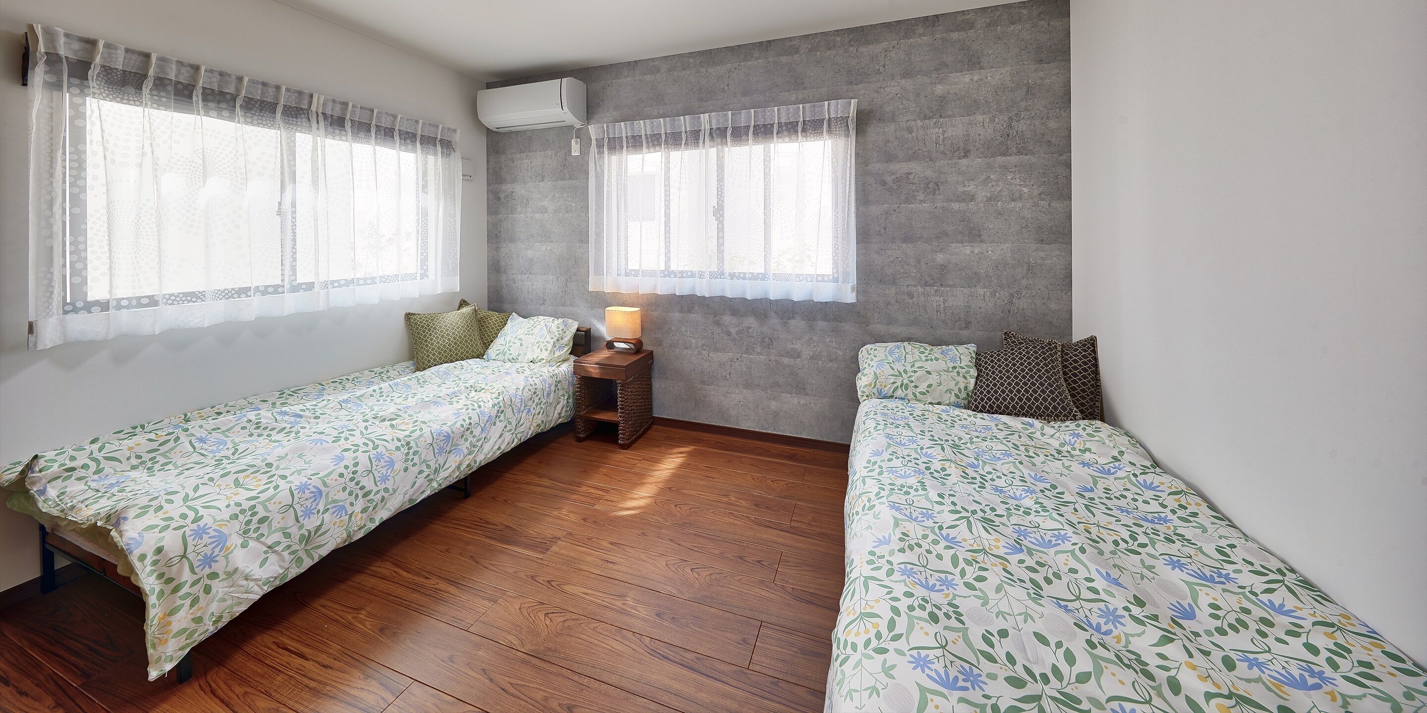 A room with two beds, a small table with a lamp, and a window with curtains.