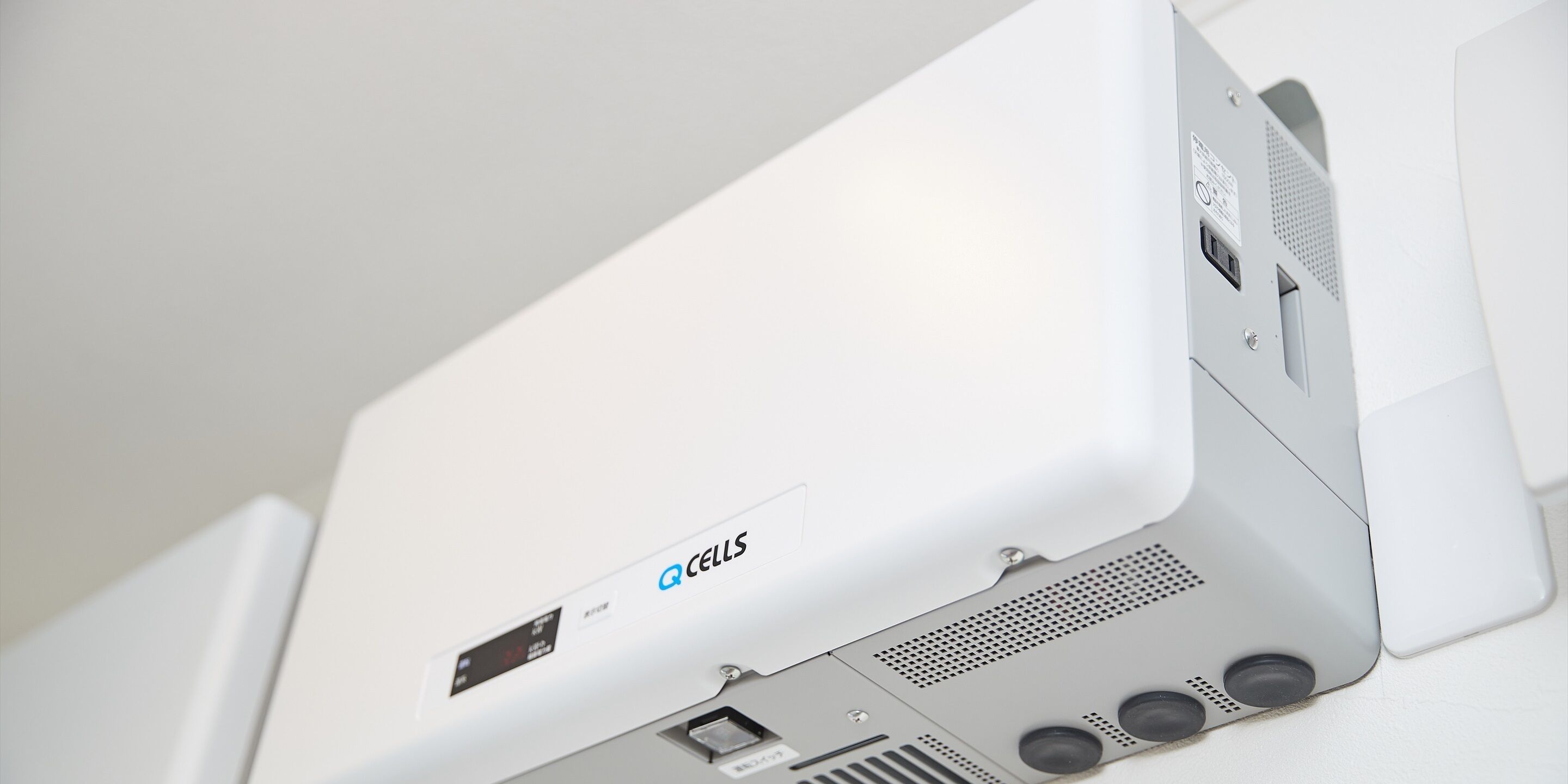 A white electronic device with a Q Cells logo, a USB port, and a speaker grille.