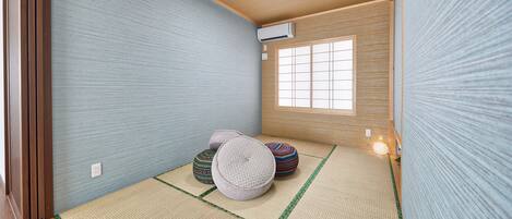 A traditional Japanese room with tatami flooring, a shoji screen, and a small tatami mat with cushions.