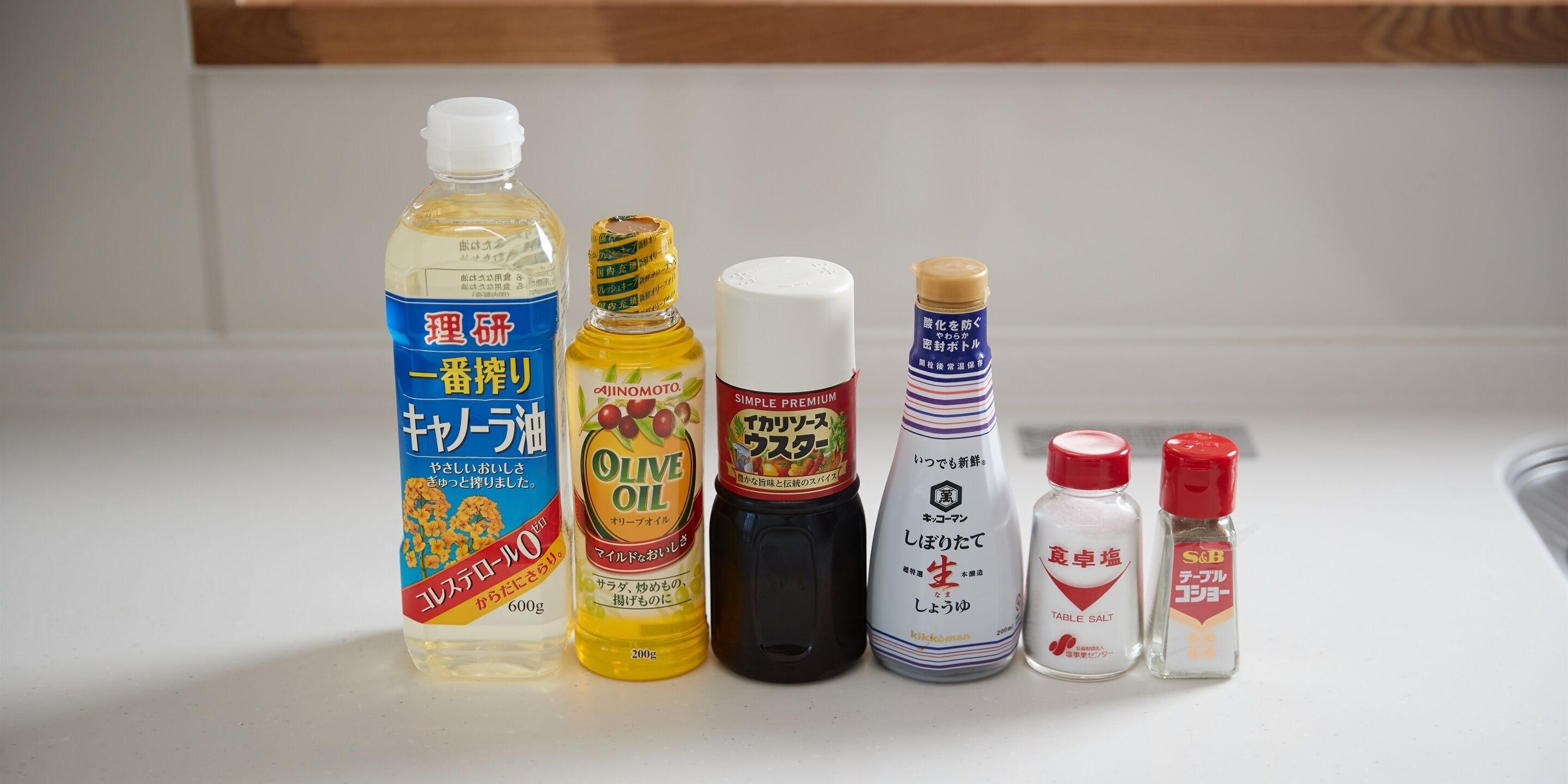 A variety of kitchen condiments including a bottle of olive oil, a bottle of soy sauce, and a bottle of table salt.