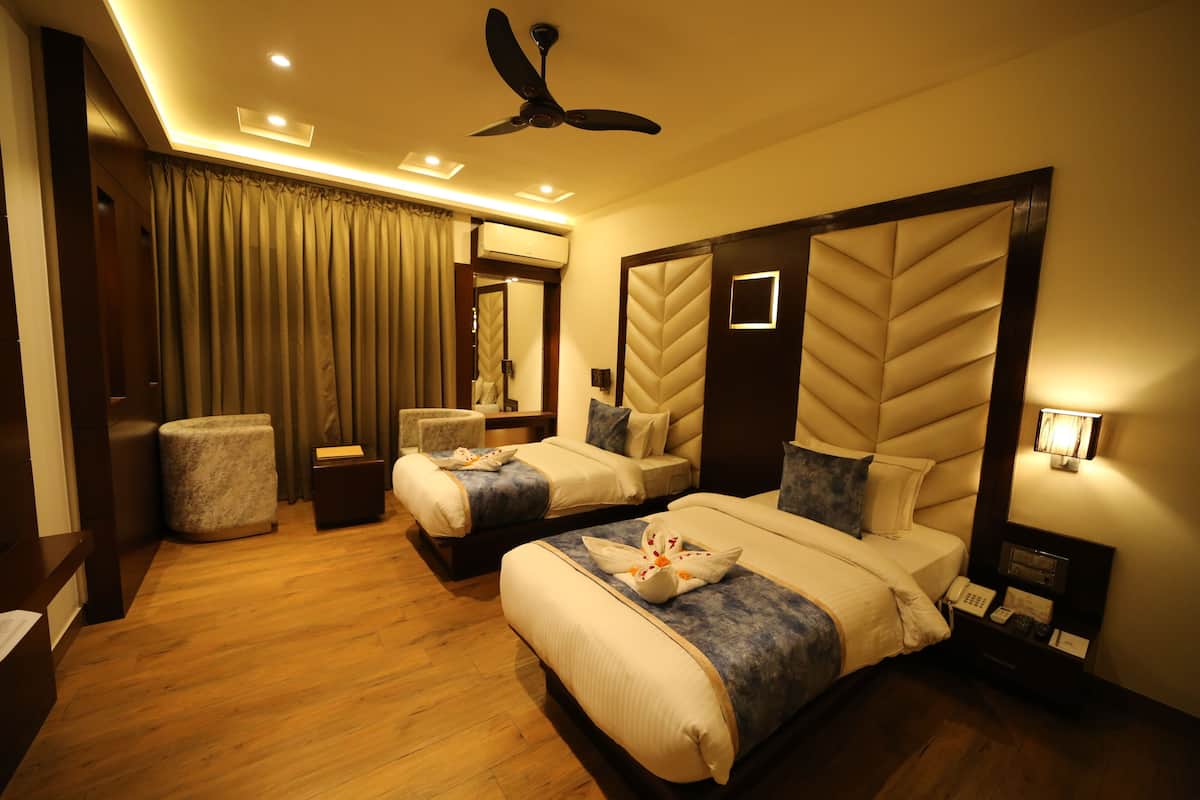 A hotel room with two beds, a ceiling fan, a bedside telephone, and a small bedside table.