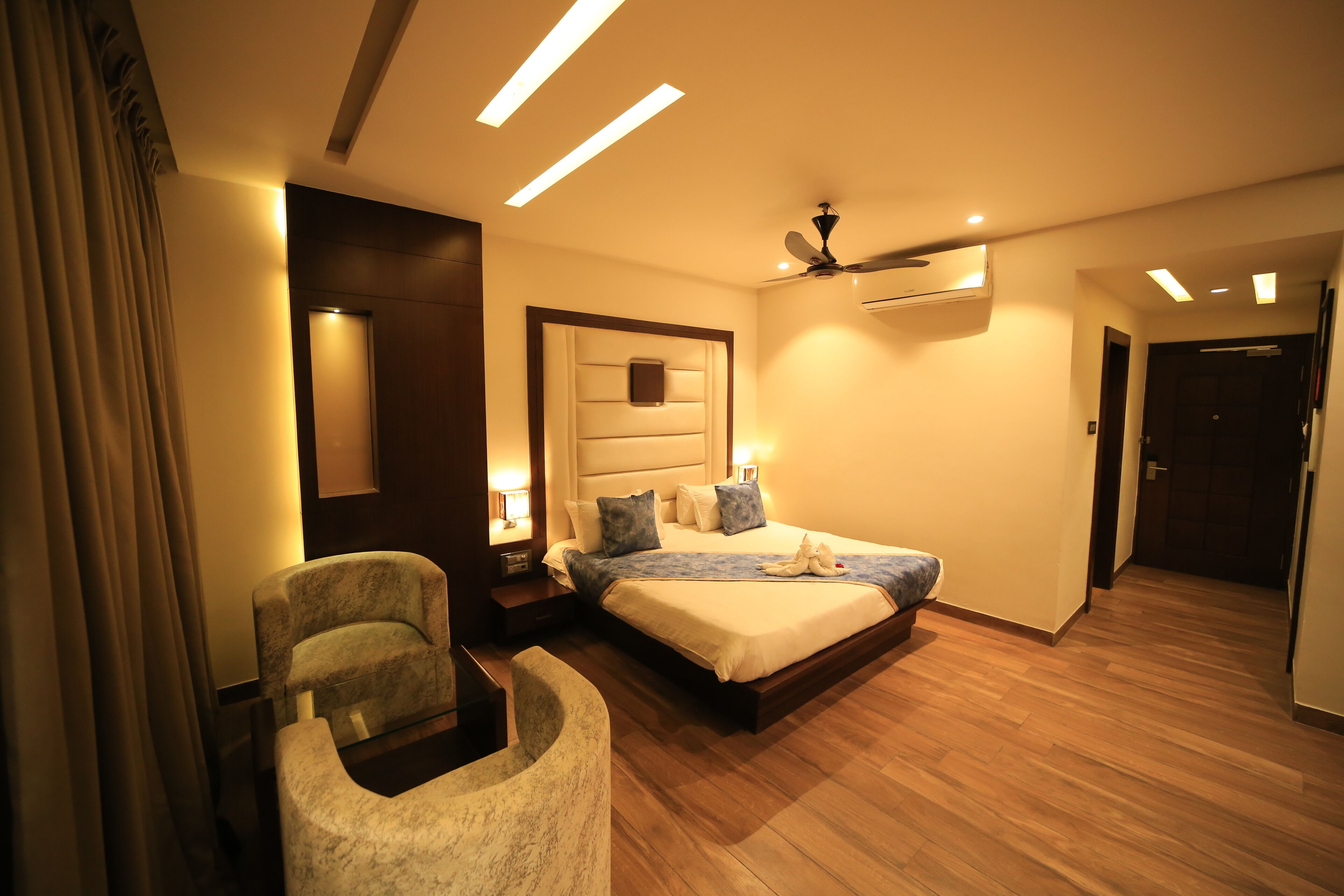 A hotel room with a bed, a chair, a ceiling fan, and an air conditioning unit.
