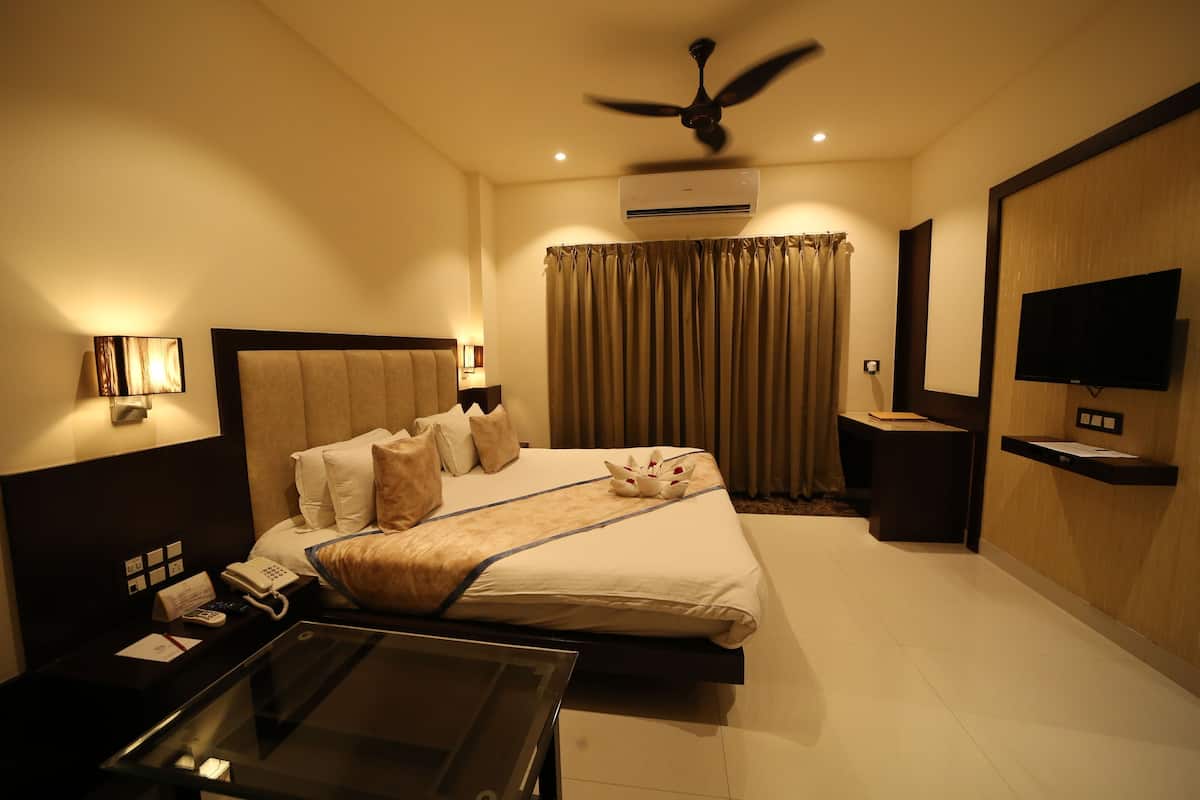 A hotel room with a bed, bedside table, lamp, air conditioning unit, TV, and curtains.