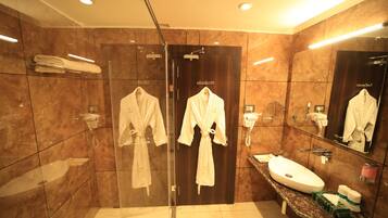 A modern bathroom with a glass-enclosed shower, a vanity with a sink, and two white robes hanging on hooks.