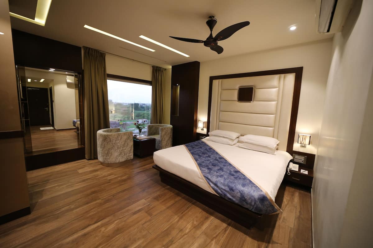A modern hotel room with a large bed, a ceiling fan, a nightstand, a bedside table, and a view of the outdoors.