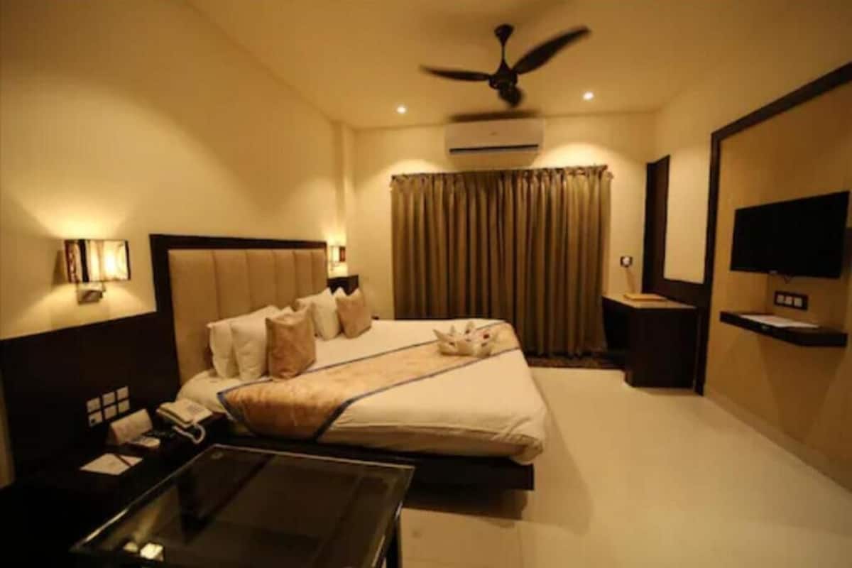 A hotel room with a bed, a desk, a chair, a TV, an air conditioner, and a ceiling fan.