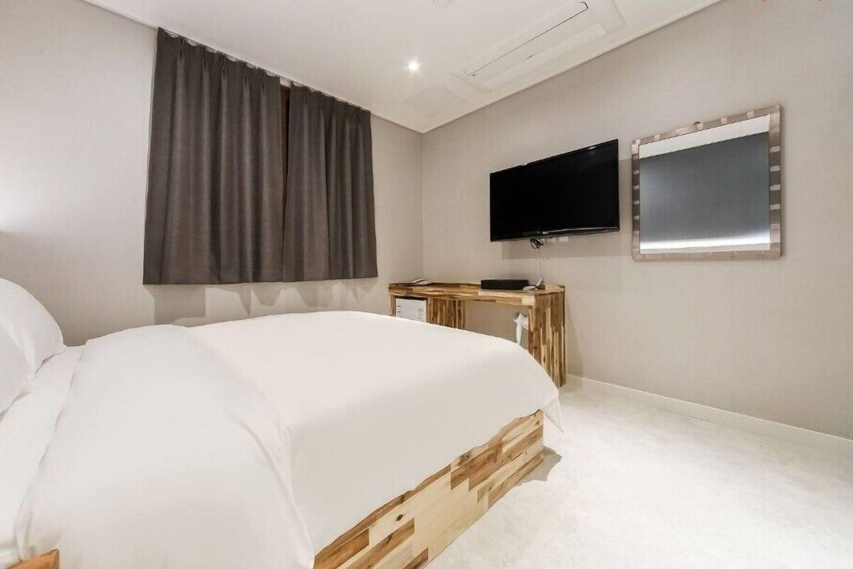 Een slaapkamer met een bed, een televisie, een spiegel en een raam met gordijnen.