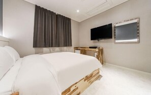 A bedroom with a bed, a TV, a mirror, and a window with curtains.