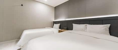 Une chambre d’hôtel moderne avec deux lits, une tête de lit sombre et une petite table de chevet.