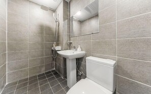 A modern bathroom with grey tiles, a white sink, a toilet, and a shower.