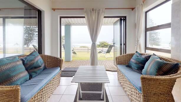 Ein sonnendurchflutetes Zimmer mit Korbmöbeln, Blick auf das Meer und einem großen Fenster.