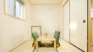 Et traditionelt japansk rum med tatamimåtter, et lavt træbord, to grønne mønstrede stole og en lille vase med blomster.