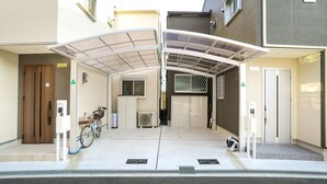 Et overdækket cykelparkeringsområde med en cykel og en scooter, en automat samt en bygningseingang.