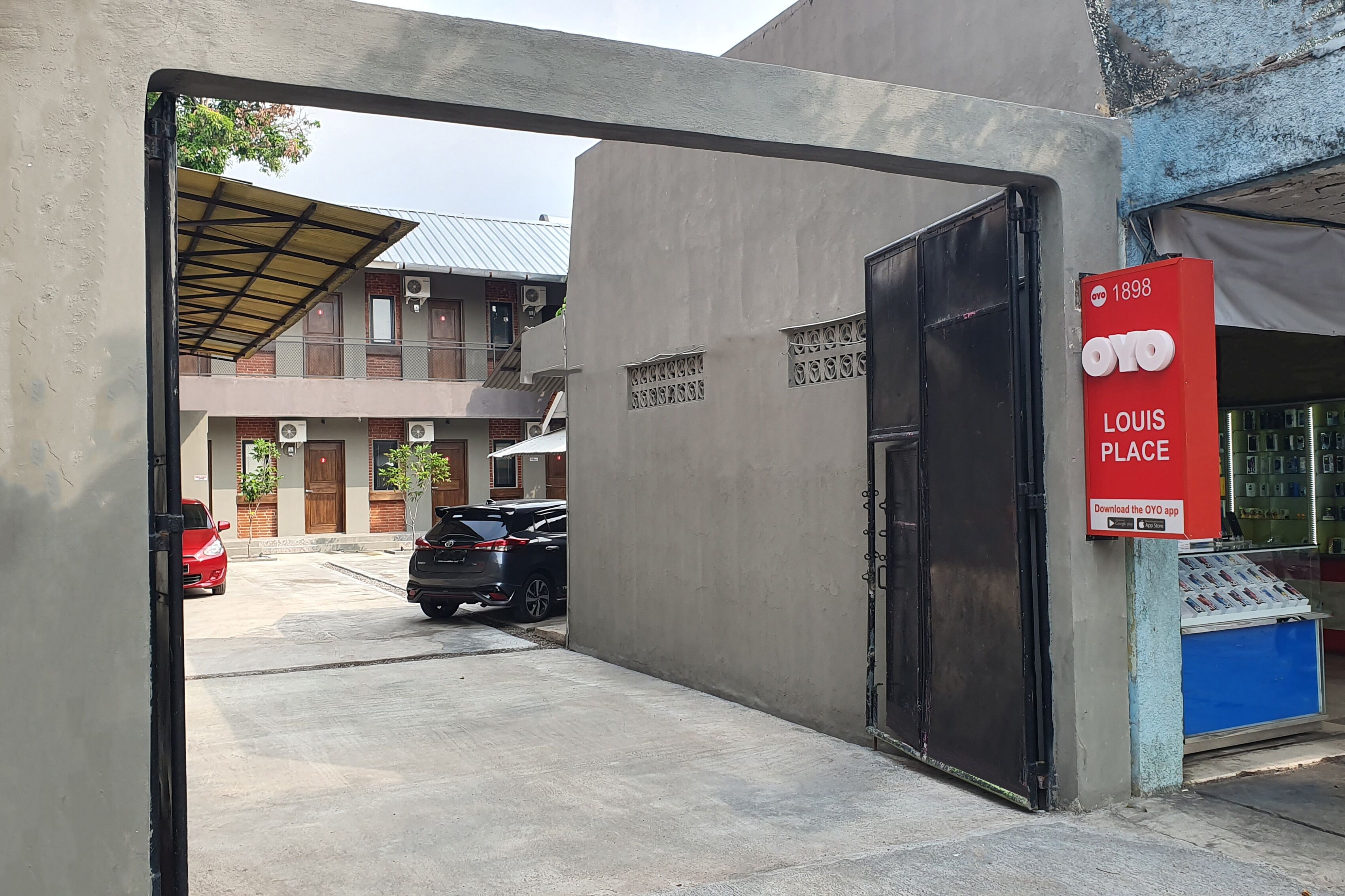 A building entrance with a metal gate, a red sign advertising OYO Place, and parked cars.