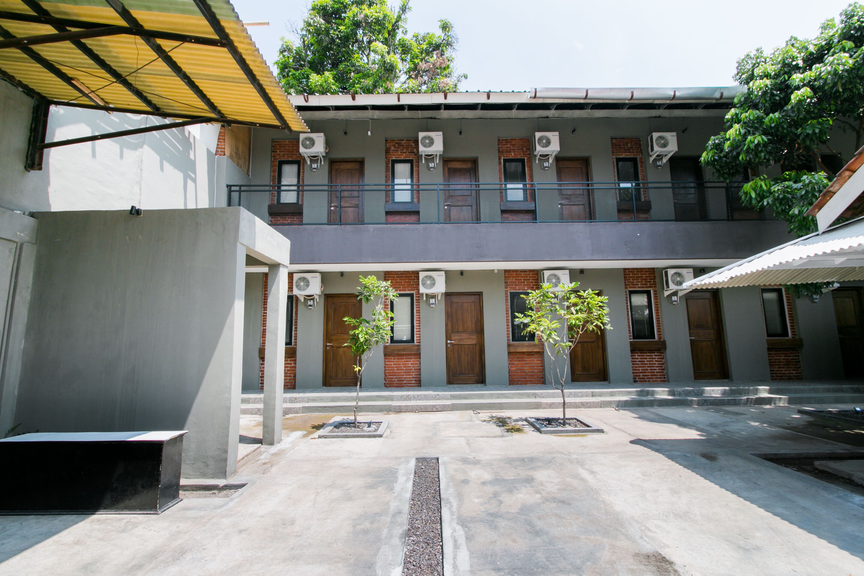 Un patio con un edificio que tiene varias unidades de aire acondicionado, piso de concreto y plantas en macetas.