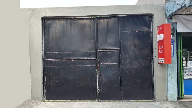 Una reja de metal negro cerrada, con un letrero rojo que dice "LOUIS PLACE" y una puerta azul a la derecha.