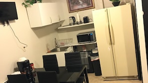 A compact kitchen with white cabinets, a microwave, a coffee maker, and a refrigerator. There is a dining table with chairs and a small potted plant on the counter. - Convenient and clean studio near the beach and Newport. (Middletown)