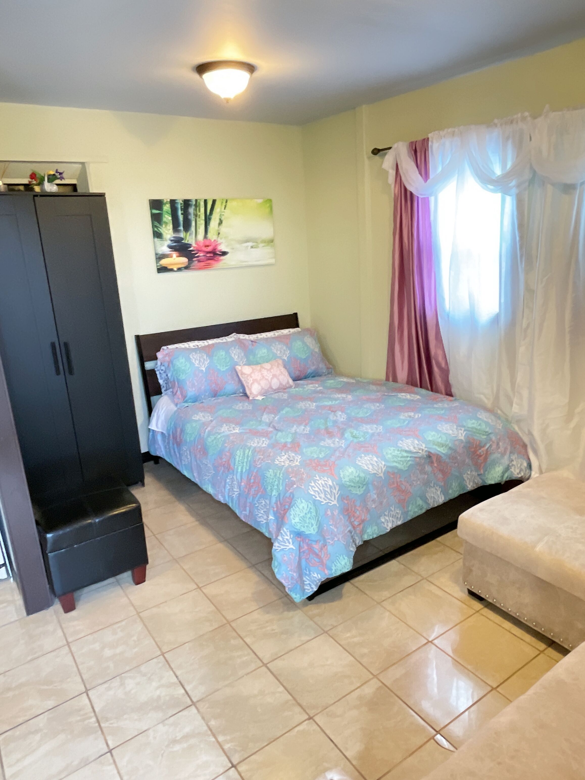 A bedroom with a bed, a nightstand, a wardrobe, and a window with curtains.