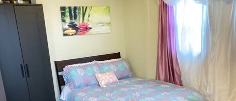 A bedroom with a bed, a nightstand, a wardrobe, and a window with curtains.