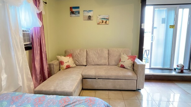 A room with a bed, a sofa, and a ceiling light. There are three paintings on the wall. - Convenient and clean studio near the beach and Newport. (Middletown)