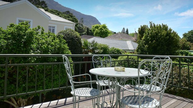 A balcony with a table and chairs, surrounded by greenery and a mountain in the background. - On Pinewood Guest House (Cape Town)
