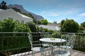 A balcony with a table and chairs, surrounded by greenery and a mountain in the background. - On Pinewood Guest House (Cape Town)