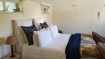 A neatly made bed with white and dark blue pillows, a blue throw blanket, and a woven chair.
