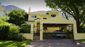 A two-story yellow house with a covered driveway and a gated entrance. - On Pinewood Guest House (Cape Town)