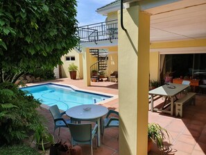 A pool area with a table and chairs, surrounded by potted plants and a staircase leading to an upper level. - On Pinewood Guest House (Cape Town)