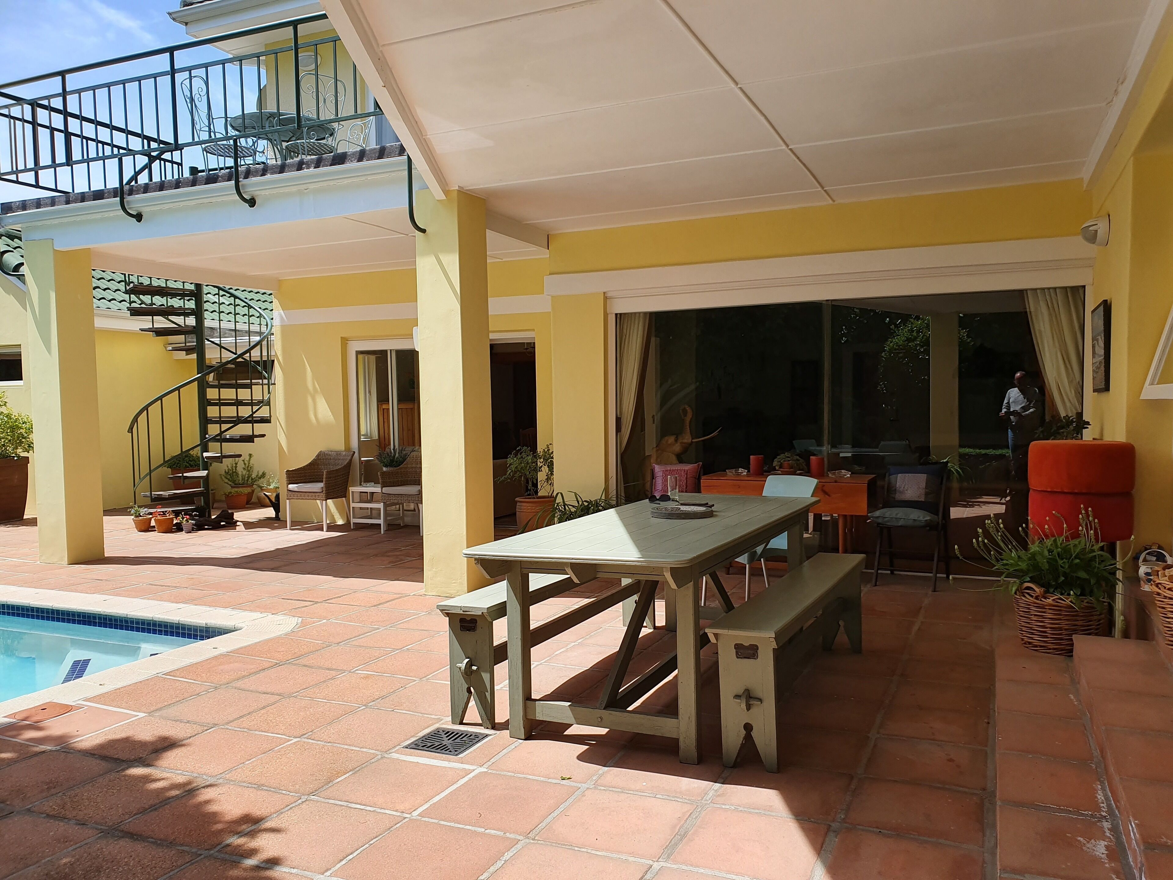 Un patio cubierto con piscina, mobiliario exterior y una escalera que lleva a un nivel superior.