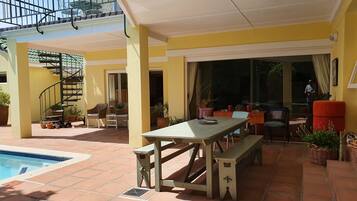Un patio cubierto con piscina, mobiliario exterior y una escalera que lleva a un nivel superior.