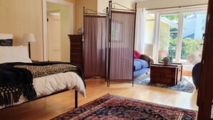 A bedroom with a bed, a nightstand, a window with curtains, a patterned rug, and a view of the outdoors. - On Pinewood Guest House (Cape Town)