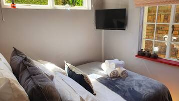 A bedroom with a bed, a TV, and a window with a view of greenery.