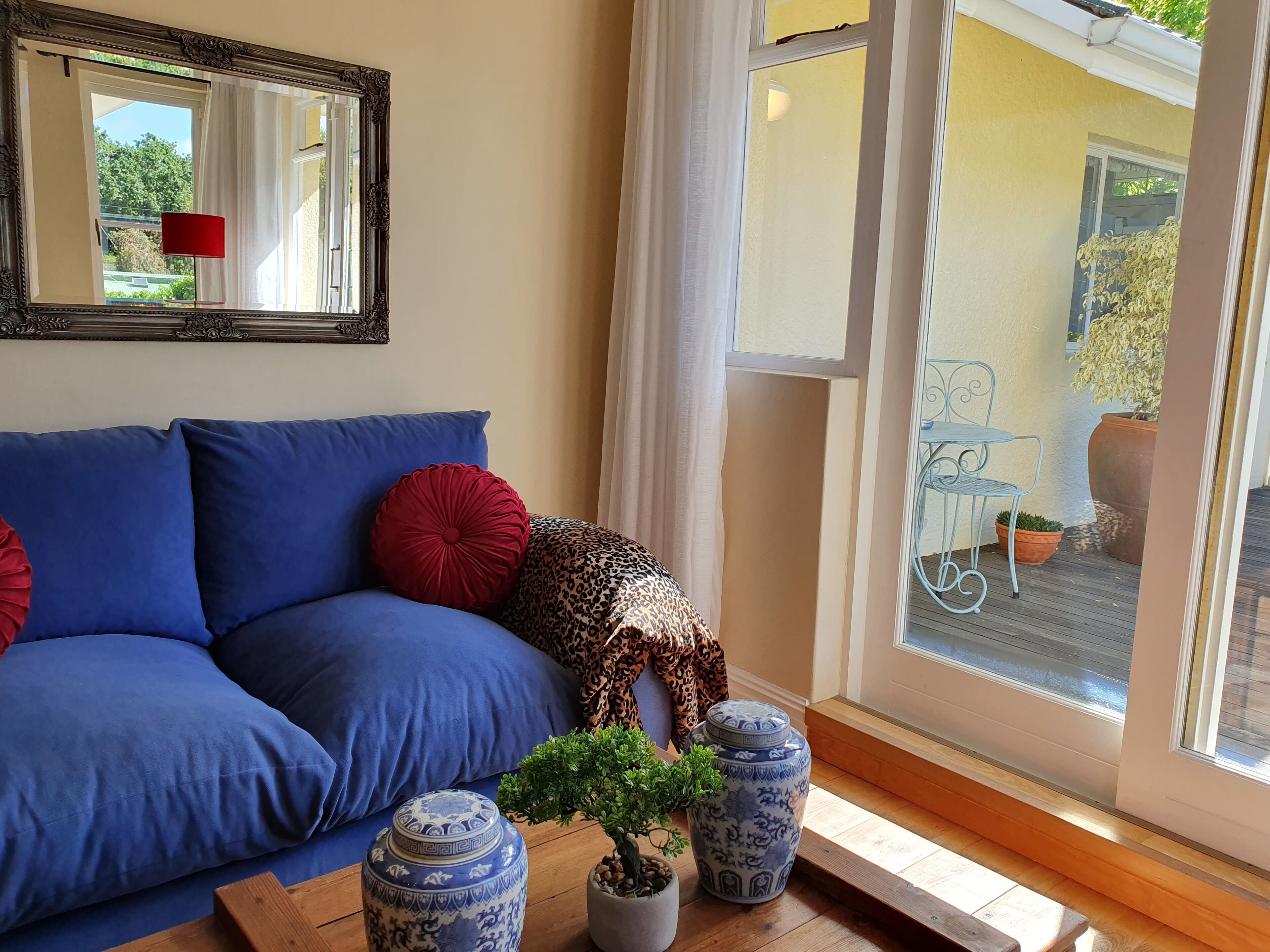 A living room with a blue sofa, decorative pillows, a mirror, and two vases with plants.