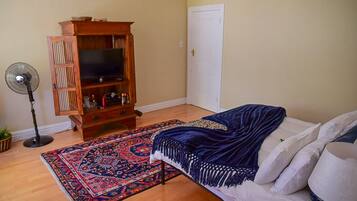 A room with a bed, a wooden entertainment unit, a standing fan, and a patterned rug.