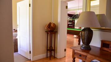 A room with a wooden floor, a lamp on a table, a door leading to another room, and a small table with a bowl.