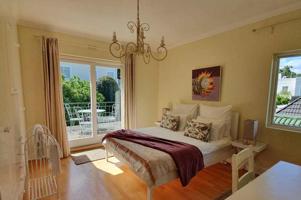 A bedroom with a bed, a chandelier, a painting, and a view of the outside.