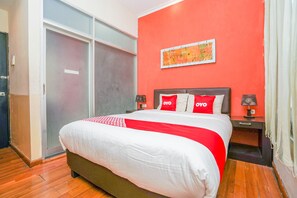 Una habitación de hotel con una cama grande, una puerta corrediza de vidrio, una pared de acento roja y una mesita de noche con lámpara.