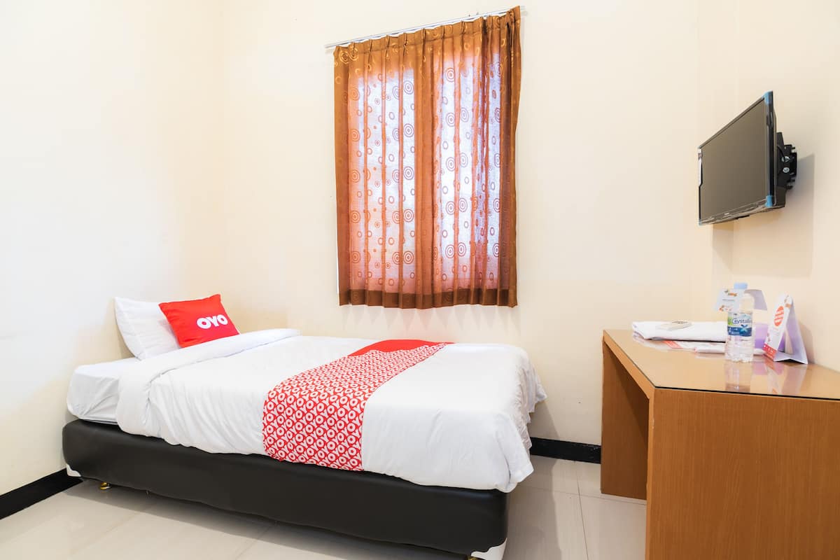 A hotel room with a bed, a desk, a television, and a window with curtains.