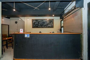 Mostrador con un menú en pizarra que enumera comida y bebidas. Se ven mesas y sillas al fondo.